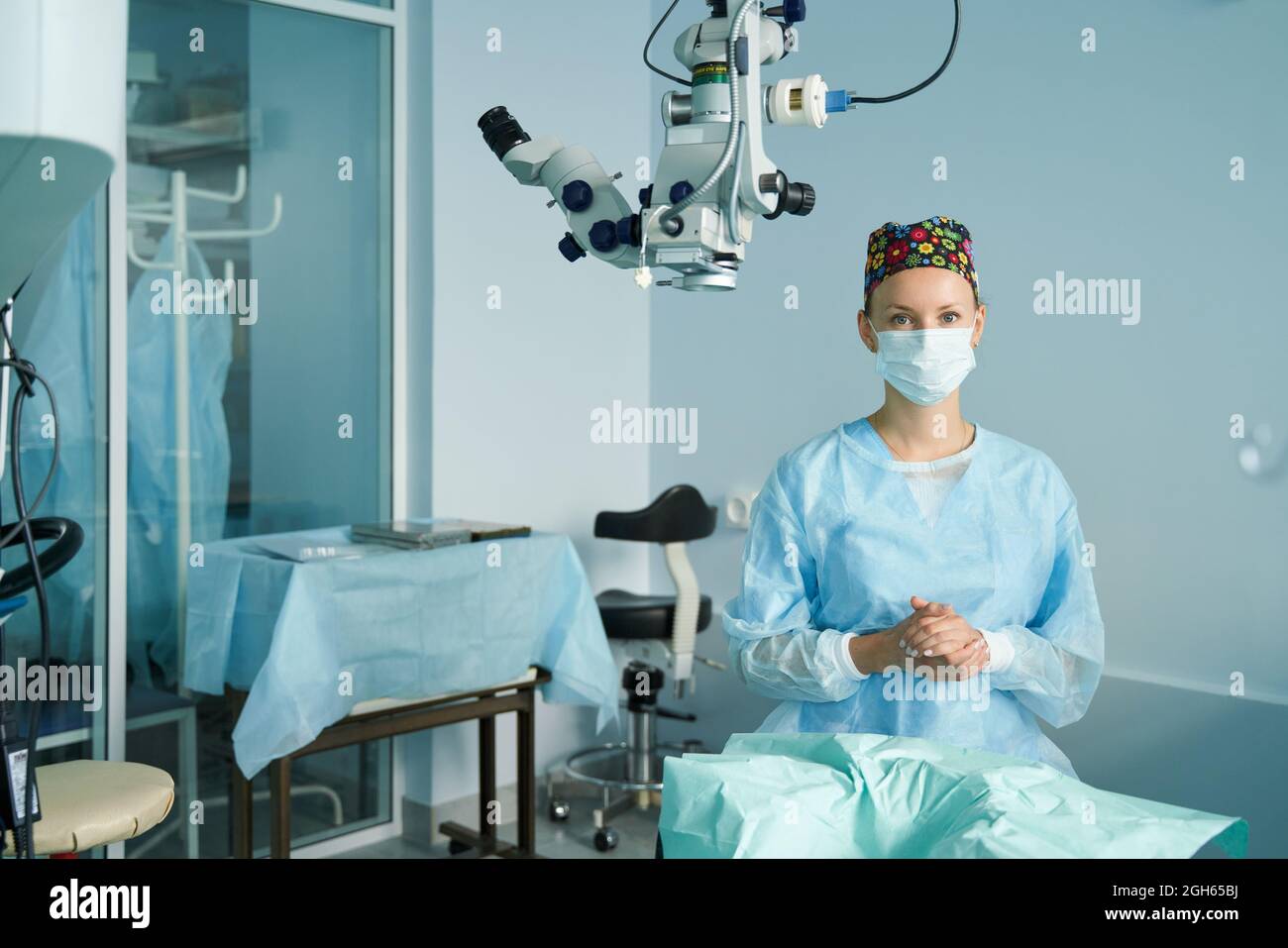 Erwachsene Ärztin in einer chirurgischen Uniform und sterilen Maske, die während des Kliniksitzens auf die Kamera schaut Stockfoto