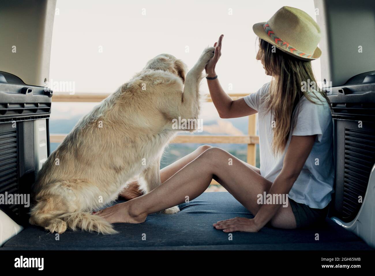Loyaler Golden Retriever Hund gibt hohe fünf zu barfuß Frau, während auf dem Bett im RV sitzen während Road Trip in der Natur Stockfoto