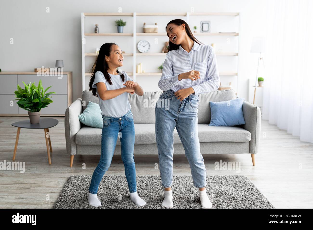 Die ganze Länge der asiatischen Mutter tanzt zu Musik mit ihrer niedlichen Tochter zu Hause, Spaß zusammen Stockfoto