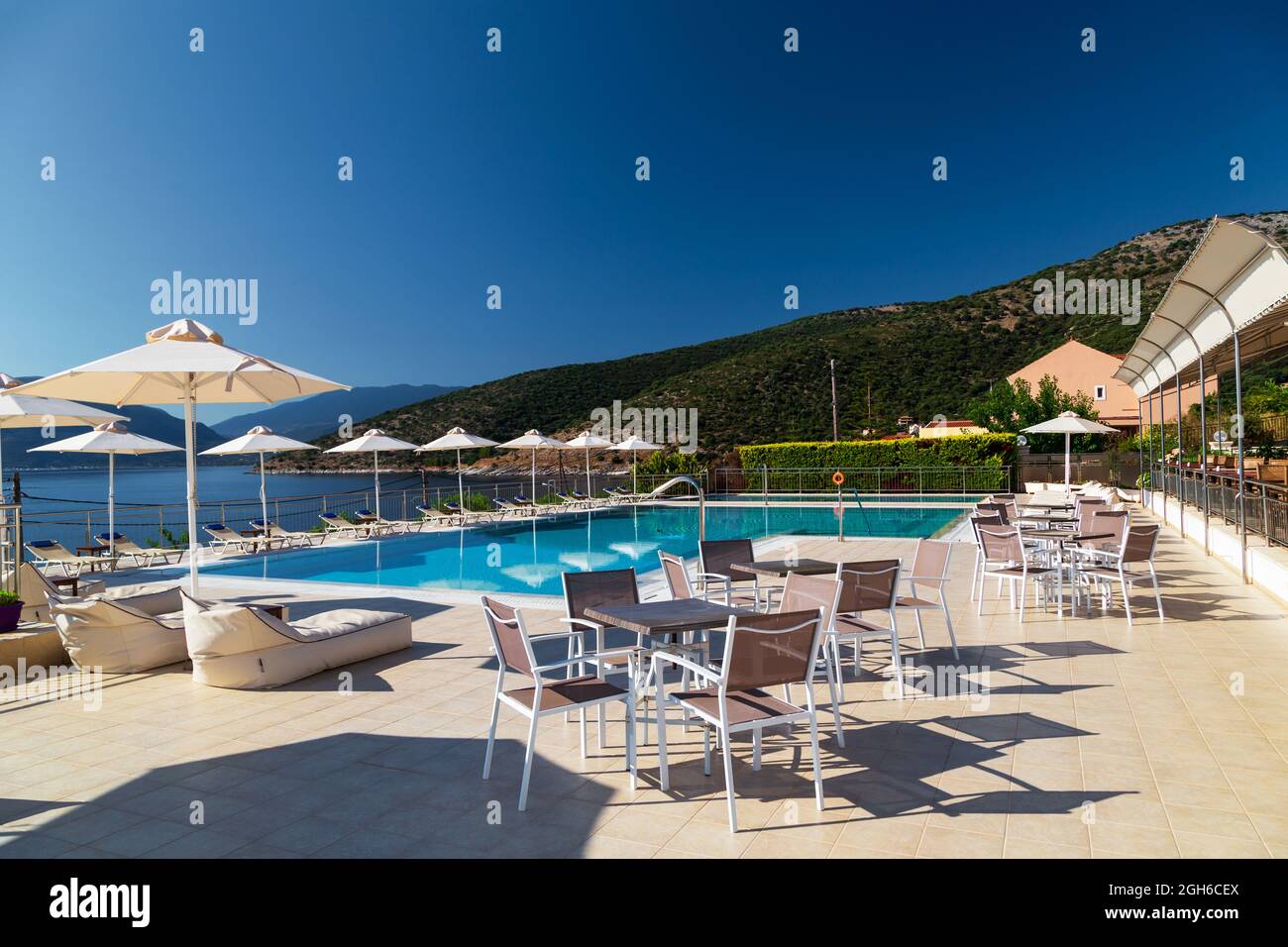 Luxus-Swimmingpool mit leeren Liegestühlen, Tischen und Sonnenschirmen im Resort mit wunderschönem Meerblick. Griechische Insel. Stockfoto