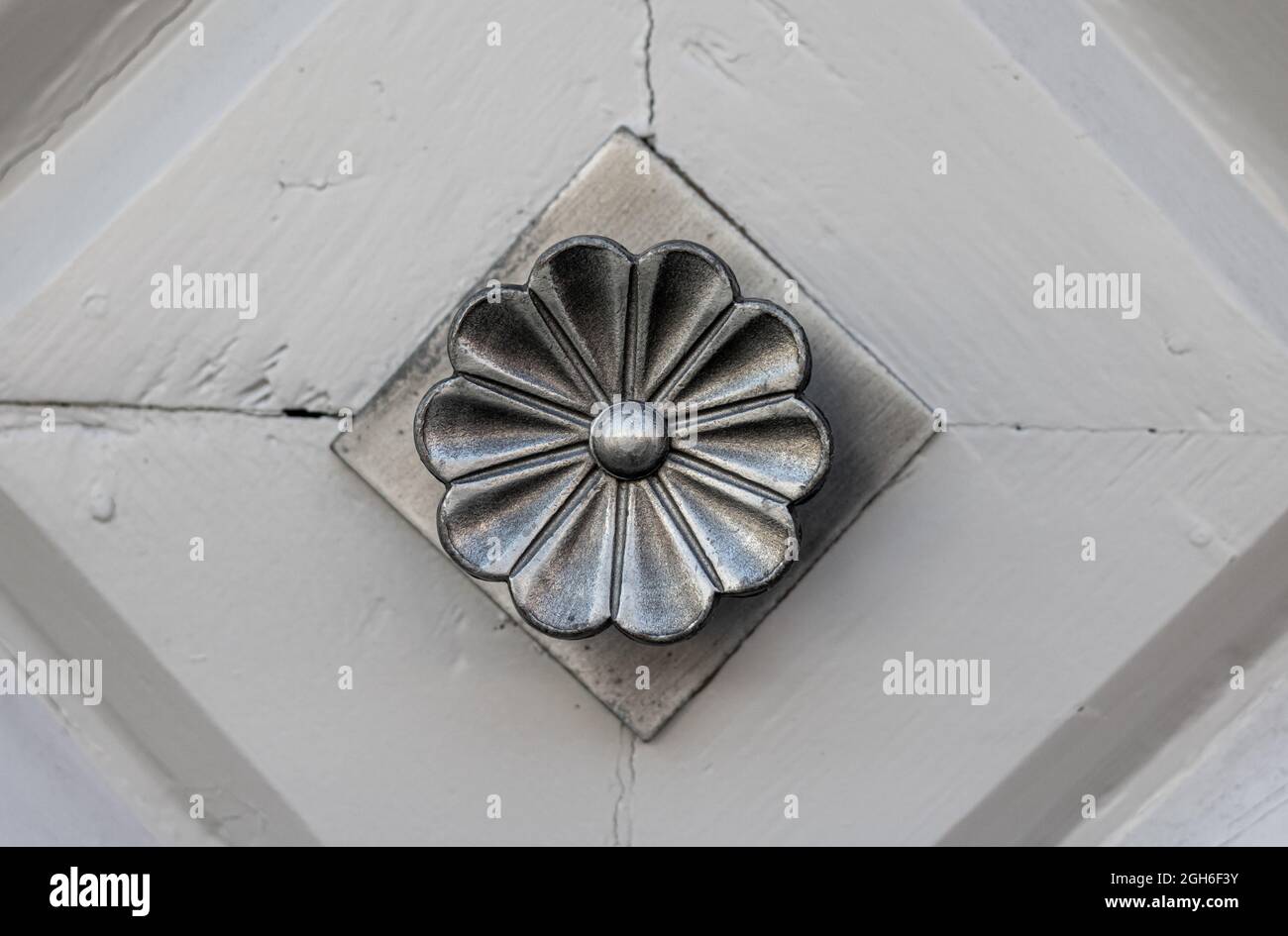 Klassischer Türknauf aus Metall mit Blumen-Optik auf einer hell gestrichenen Tür mit Rautenmustern Stockfoto