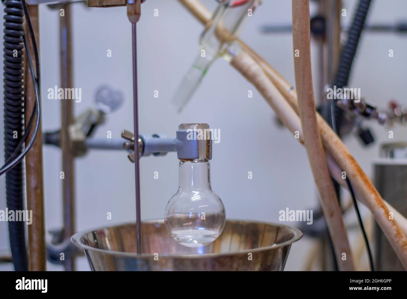 Rundkolben mit transparenter Flüssigkeit für die chemische Synthese in einem Chemielabor mit elektrischer Einrichtung Stockfoto