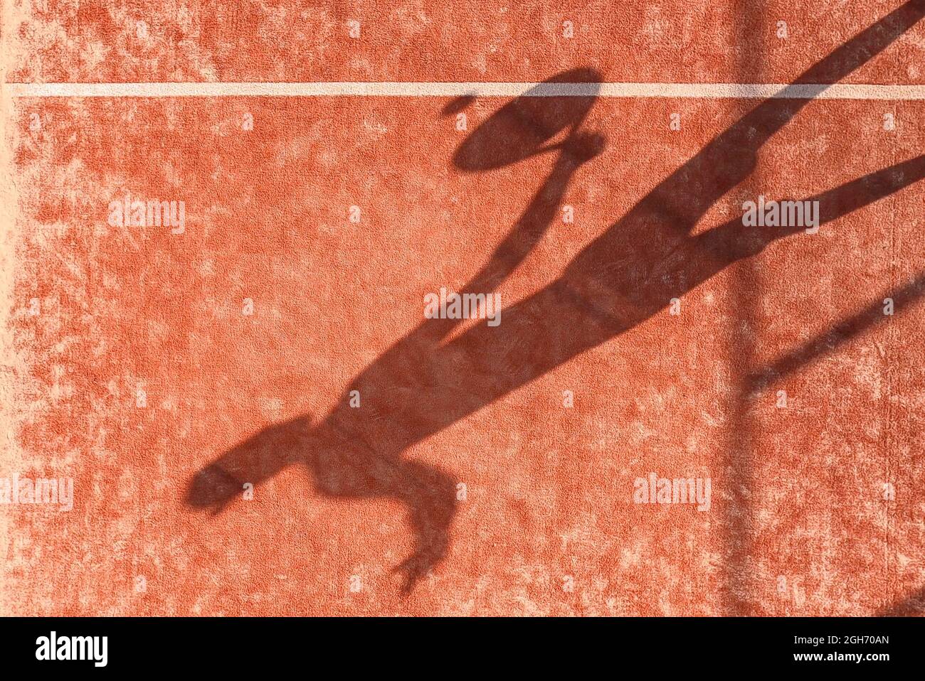 Der Schatten eines Paddle-Tennisspielers mit einem Schläger in der Hand, der den Ball auf einem Platz im Freien trifft. Stockfoto