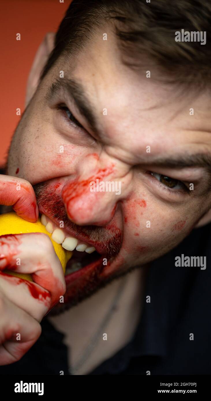 Ein Kerl beißt eine Zitrone auf einem roten Hintergrund . Nahaufnahme Porträt Stockfoto