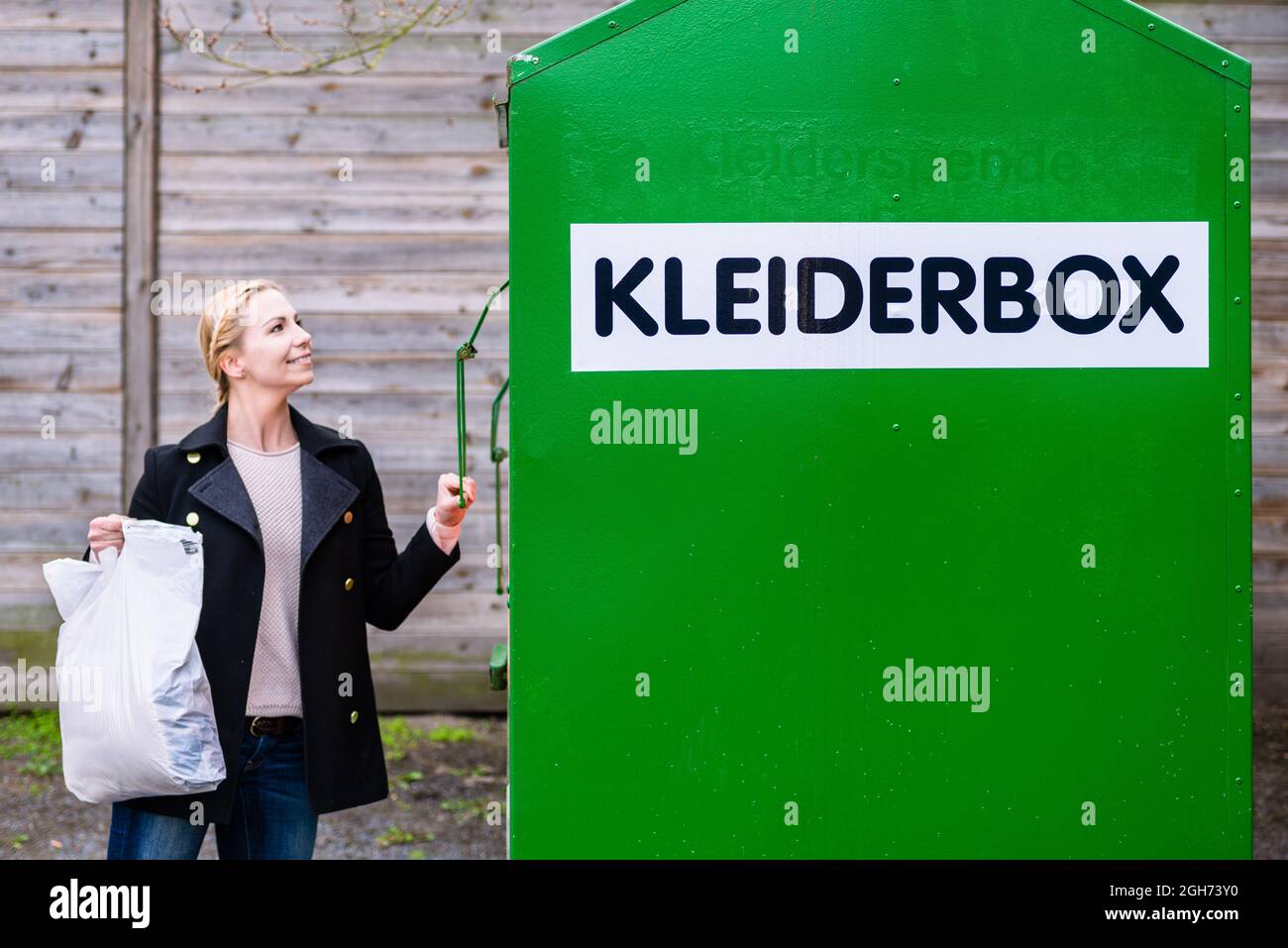 Frau, die alte oder gebrauchte Kleidung in den Spendenbehälter legt Stockfoto