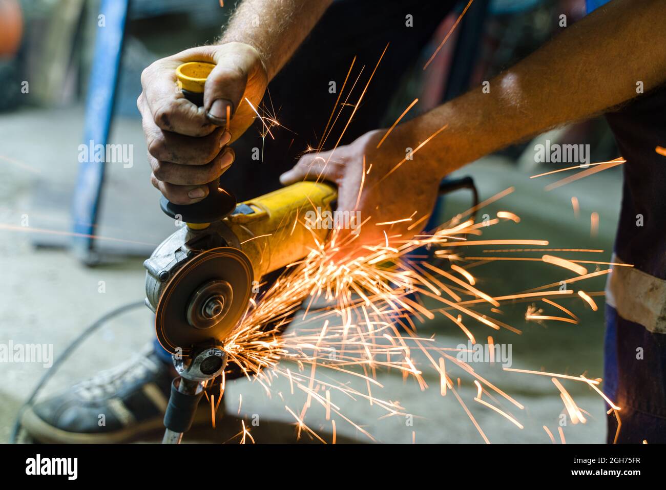 Schlosser in Spezialkleidung und Brille arbeitet in der Produktion. Metallverarbeitung mit Winkelschleifer. Funken bei Metallarbeiten Stockfoto