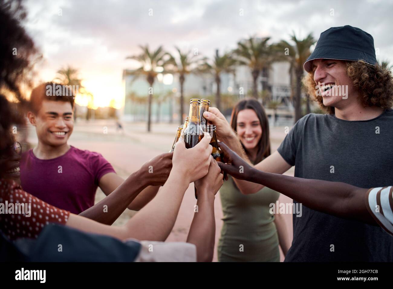 Eine Gruppe junger Menschen mit einem schönen Lächeln toastt den Sonnenuntergang. Glückliche gemischte Rennfreunde, die Spaß haben. Stockfoto