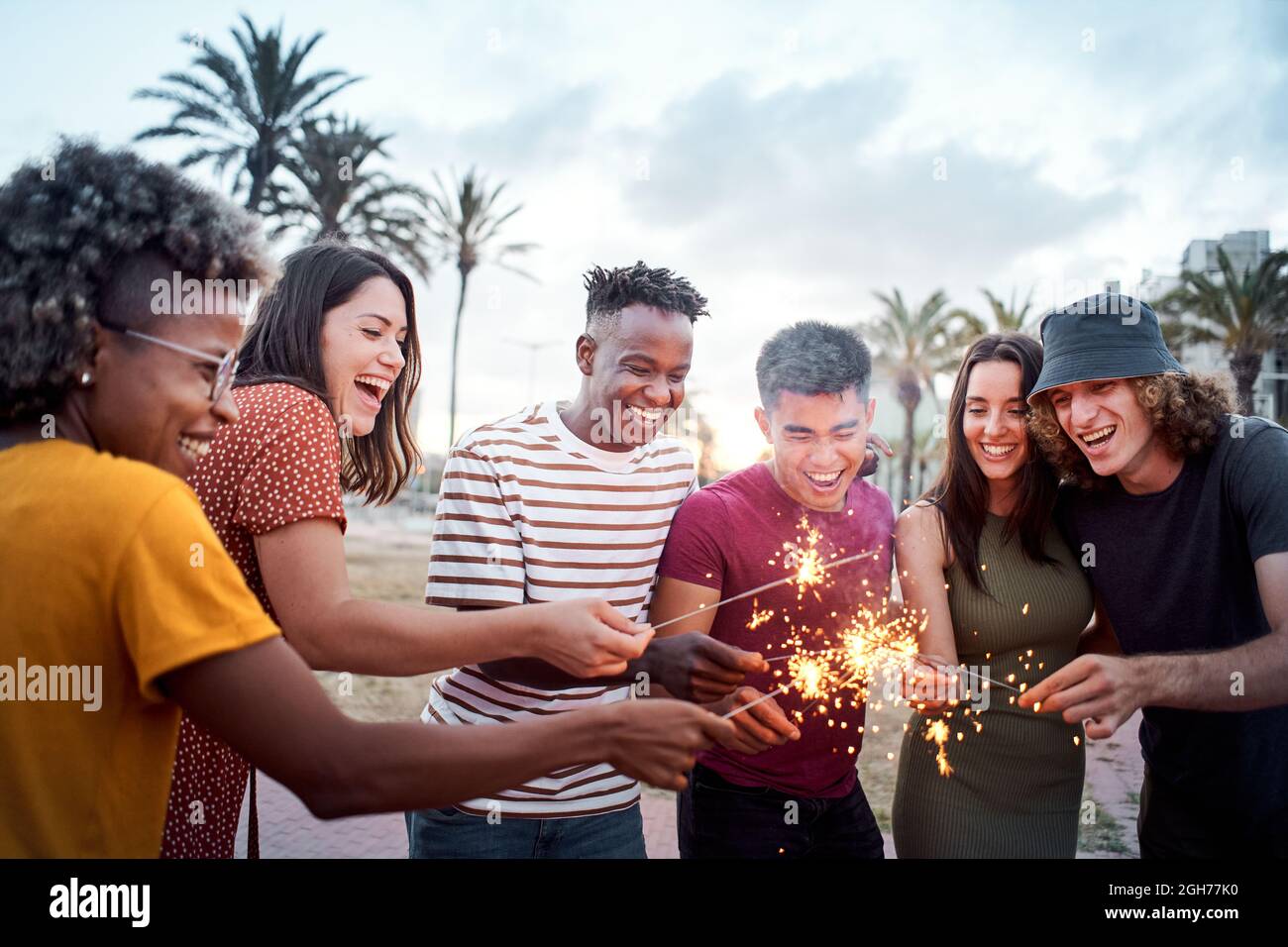 Eine Gruppe von Freunden, die lächeln und sich um einige Wunderkerzen herum Vergnügen. Im Sommer verbringen junge Leute gerne Zeit miteinander. Konzept von Stockfoto