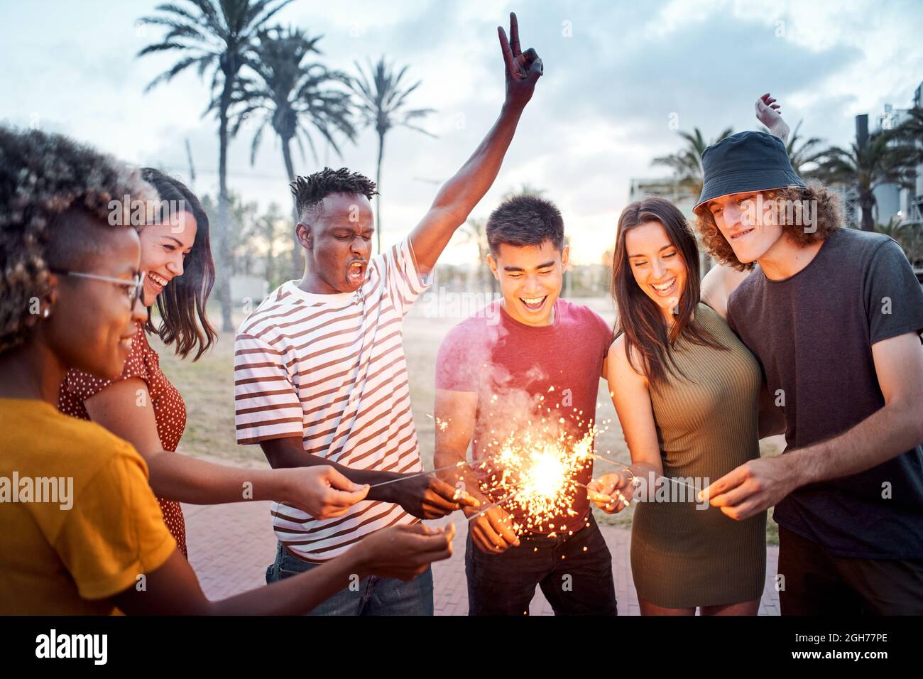 Eine Gruppe von Freunden zünden bei Sonnenuntergang einige Wunderkerzen an. Junge Multiethniker feiern gemeinsam. Konzept von Sommer, Integration, Glück, Freizeit Stockfoto