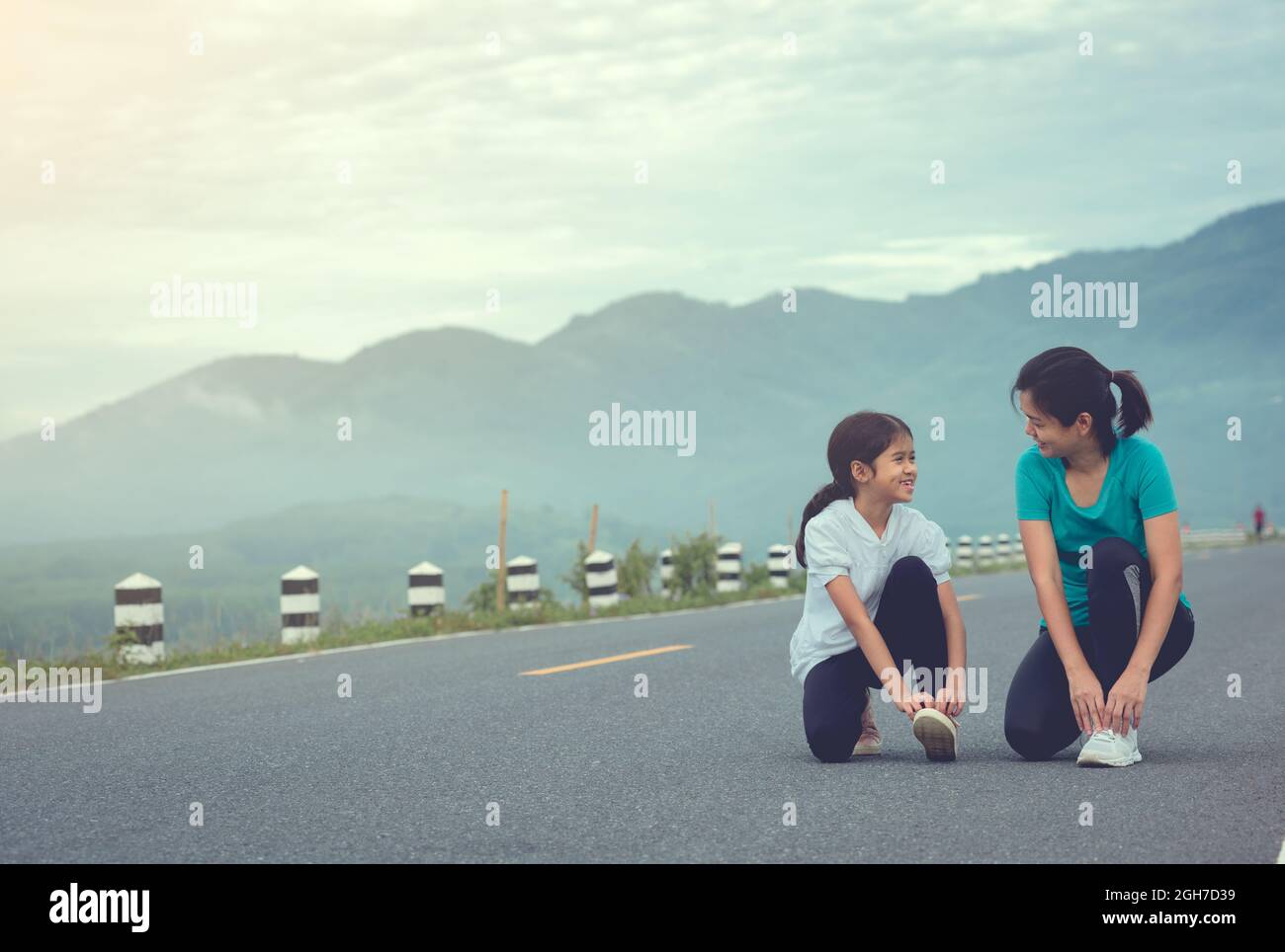 Mutter und Kind knien und binden Schnürsenkel. Wir machen uns bereit zum Joggen im Freien während des Sonnenaufgangs auf der Staudamm-Straße zu trainieren. Stockfoto