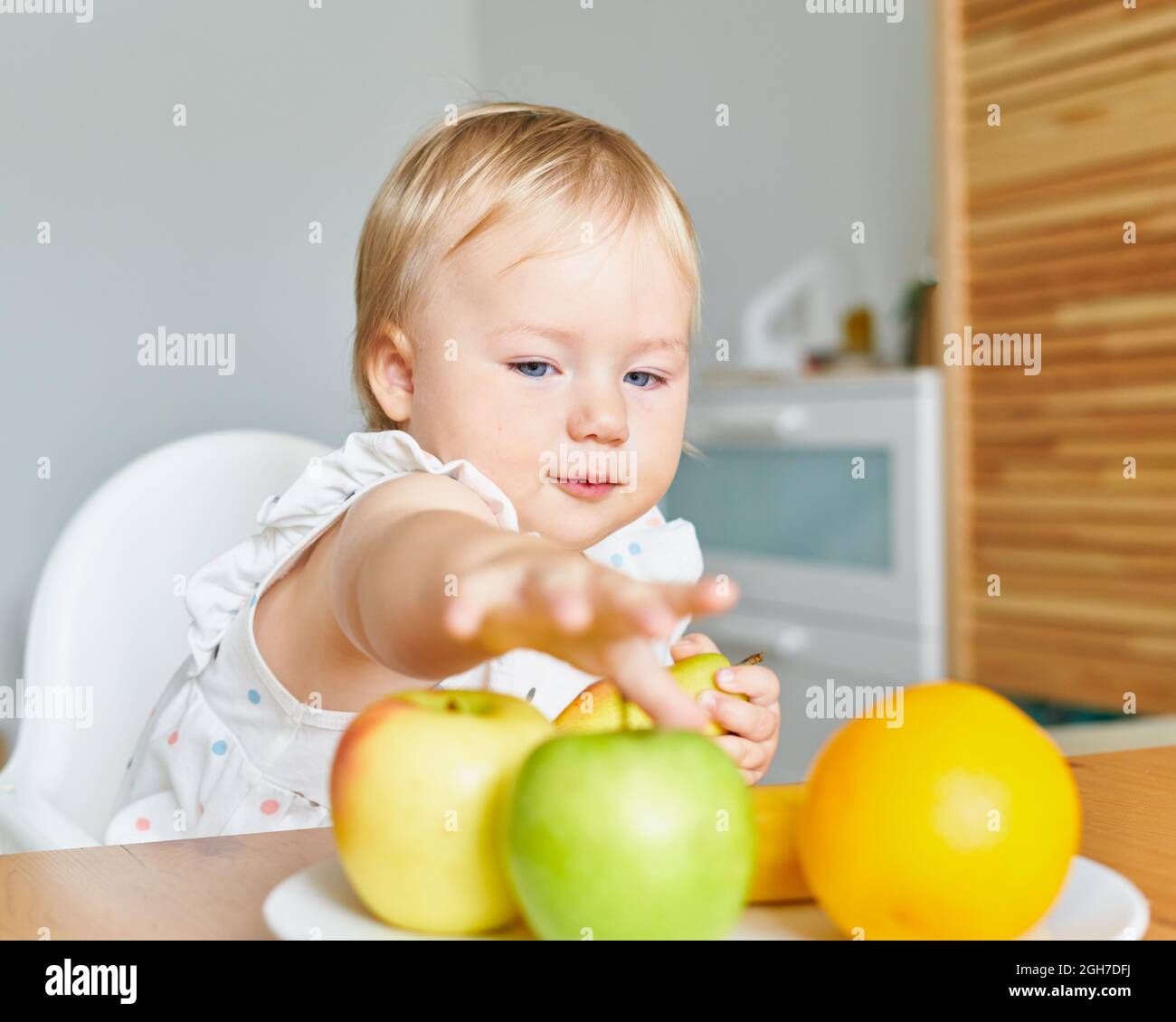 Schönes Baby suchen und greifen nach Früchten auf dem Teller. Gesunde Essgewohnheiten. Stockfoto