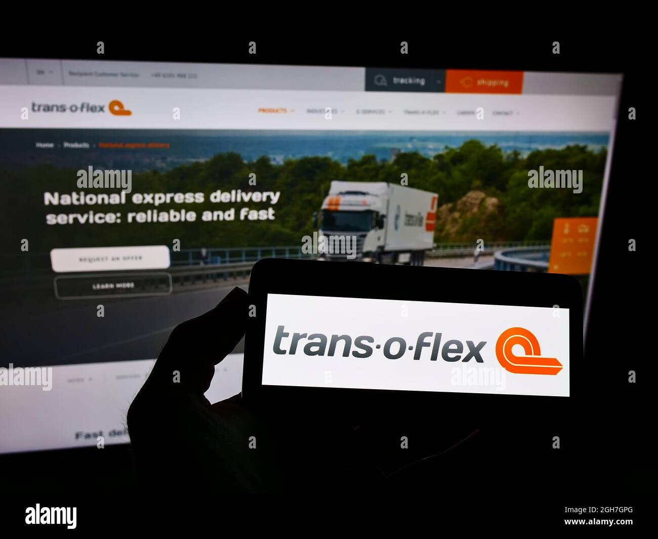 Person, die Smartphone mit Logo des deutschen Logistikunternehmens trans-o-Flex Express GmbH auf dem Bildschirm vor der Website hält. Konzentrieren Sie sich auf die Telefonanzeige. Stockfoto