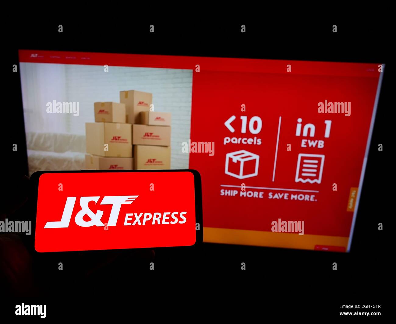 Person mit Mobiltelefon und Logo des indonesischen Unternehmens PT Global Jet Express (JT) auf dem Bildschirm vor der Business-Webseite. Konzentrieren Sie sich auf die Telefonanzeige. Stockfoto