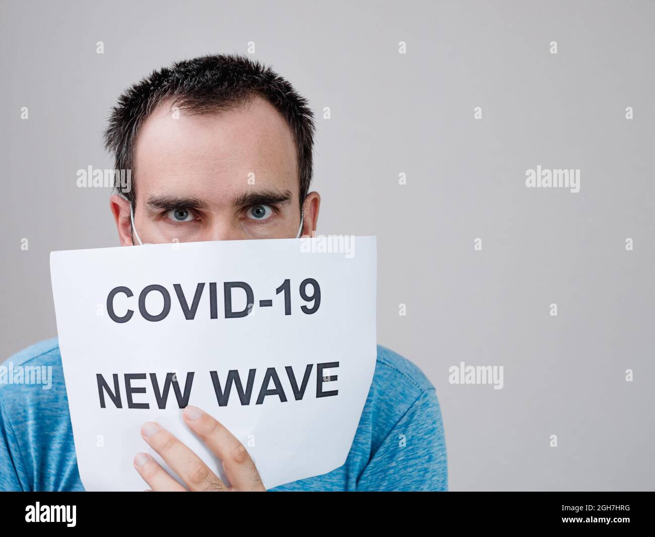 Ein kaukasischer Mann bedeckte die Hälfte seines Gesichts mit einem Blatt, das lautete: Covid -19 New wave. Das Konzept der Bekämpfung der Epidemie Stockfoto