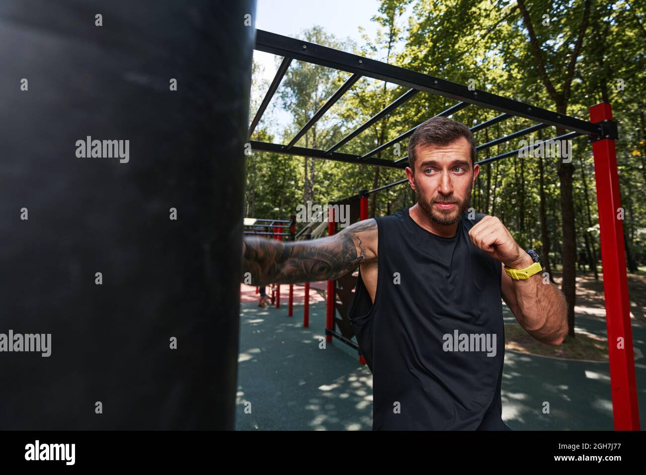 Ein gutaussehender, starker Rüde trainiert im Freien auf Sportplatz und tritt Boxsack Stockfoto