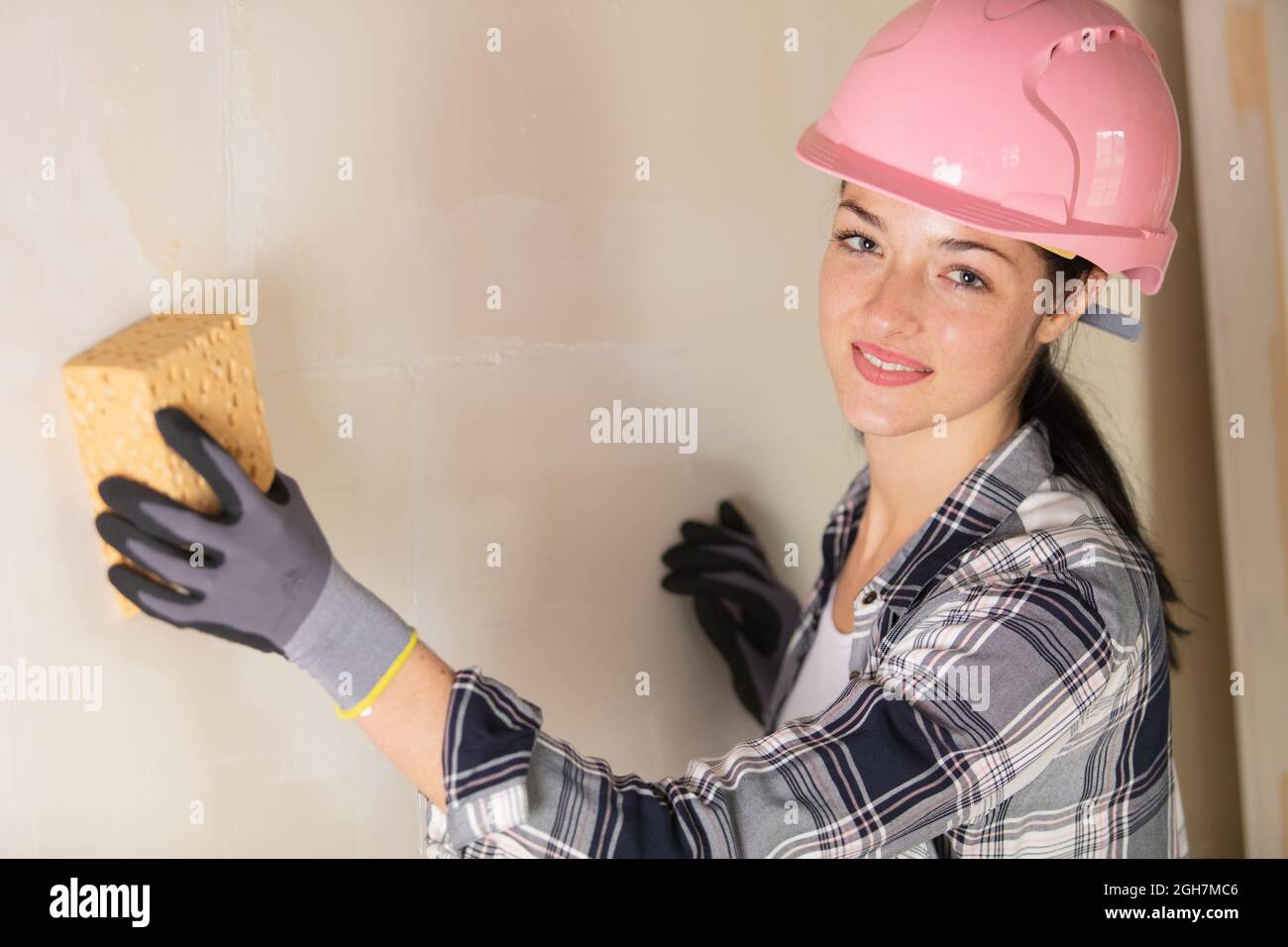 Weibliche Builder mit Schwamm an der Wand Stockfoto