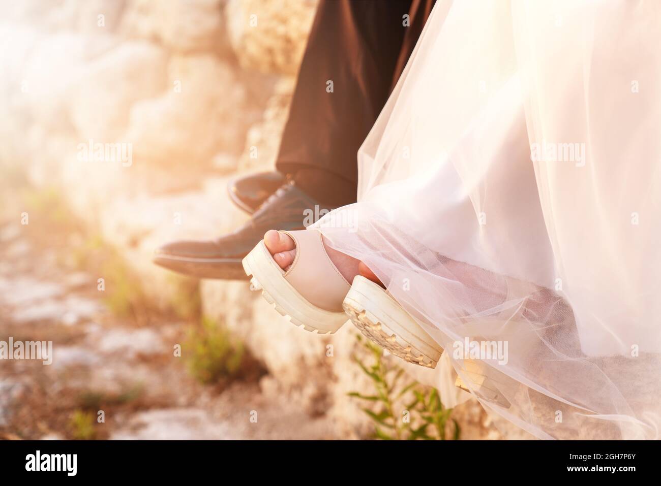 Braut und Bräutigam sitzen nach einem aufgeregt erschöpften Hochzeitstag zusammen mit Beinen und Schuhen. Hochwertige Fotos Stockfoto