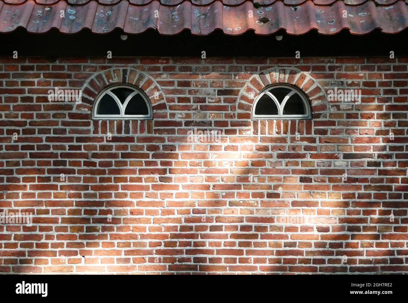 Eine alte gemauerte Wand mit zwei Bogenfenstern und einem Ziegeldach. Gesehen in den Niederlanden Stockfoto