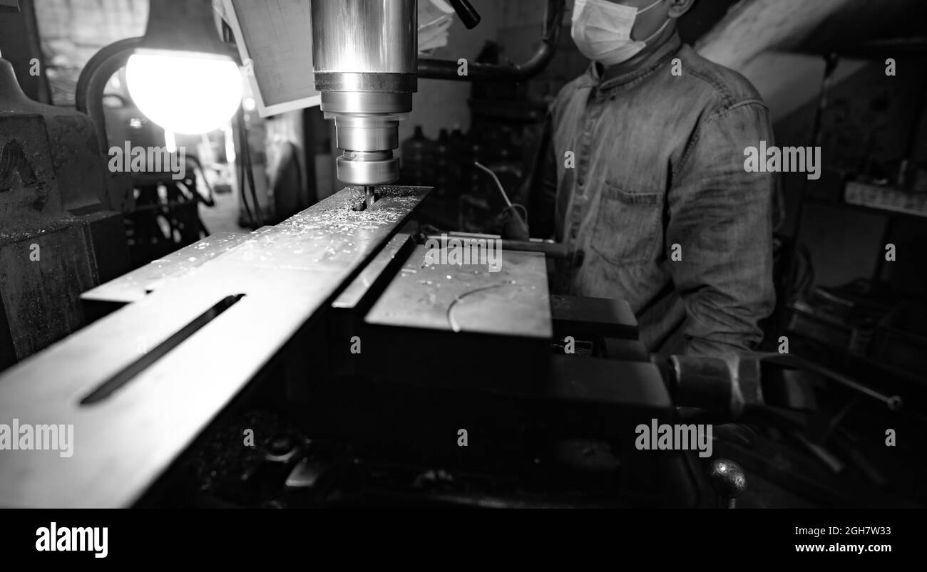 Fräsmaschine, die in der Nähe des Arbeiters mit einer Schutzmaske arbeitet. Werkzeug zum Schneiden von Metallwerkstücken. Vertikale Fräsmaschine mit Wolfram Hartmetall Fräsen Stockfoto