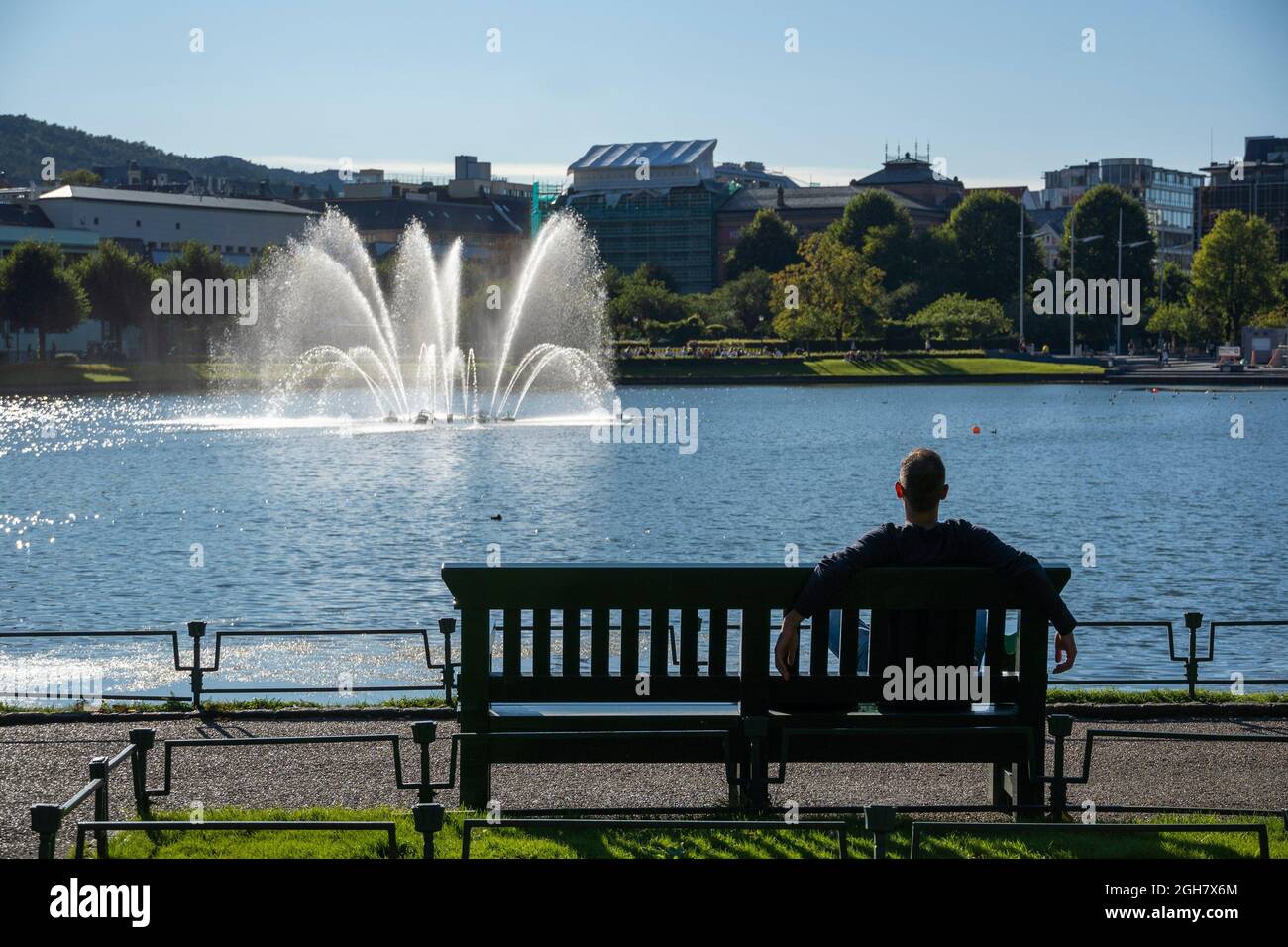 Mann sitzt auf einer Parkbank und genießt die Sonne neben Lille Lungegårdsvannet oder Smålungeren, einem kleinen See im Zentrum der Stadt Bergen, Norwegen Stockfoto