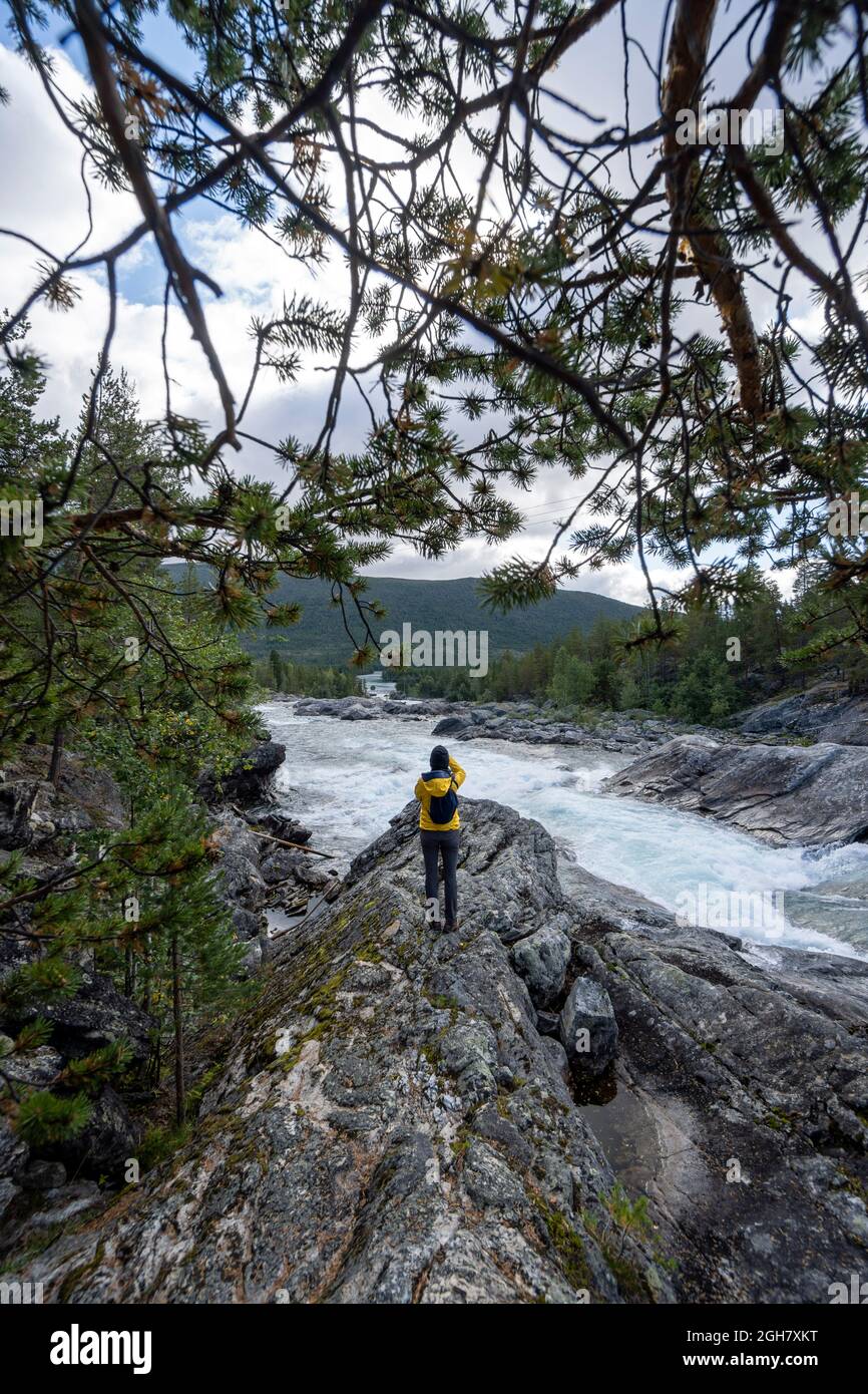 Rückansicht einer Person in einer gelben Jacke, die Fotos vom Pollfoss-Wasserfall, dem Fluss Otta, Oppland, Norwegen, macht Stockfoto