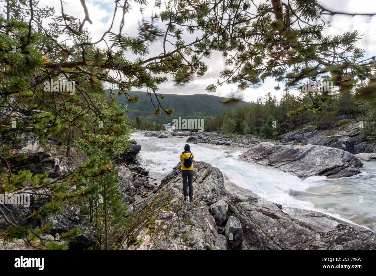 Rückansicht einer Person in einer gelben Jacke, die Fotos vom Pollfoss-Wasserfall, dem Fluss Otta, Oppland, Norwegen, macht Stockfoto