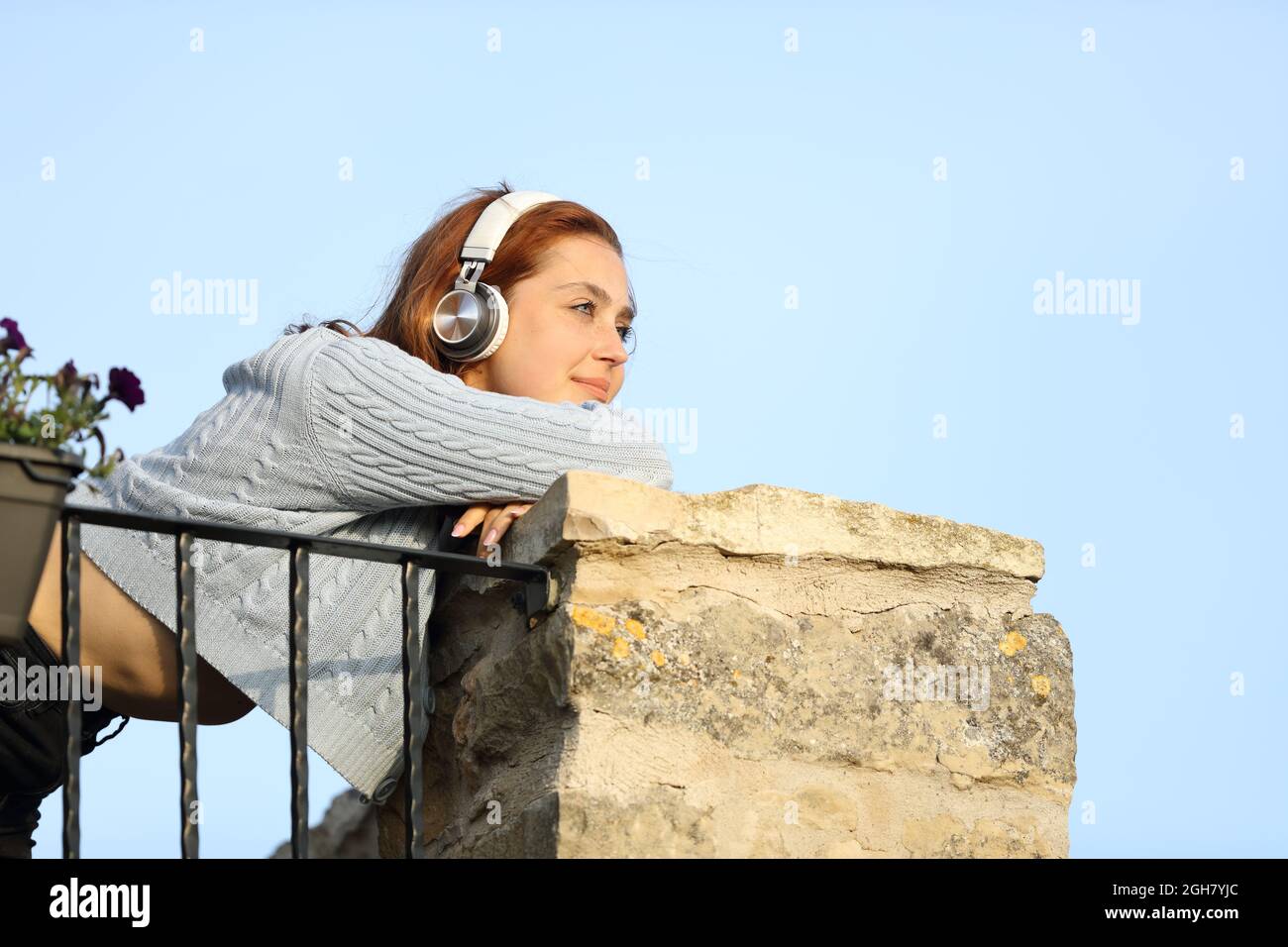 Glückliche Frau, die vom Balkon aus mit Kopfhörern Musik hört Stockfoto