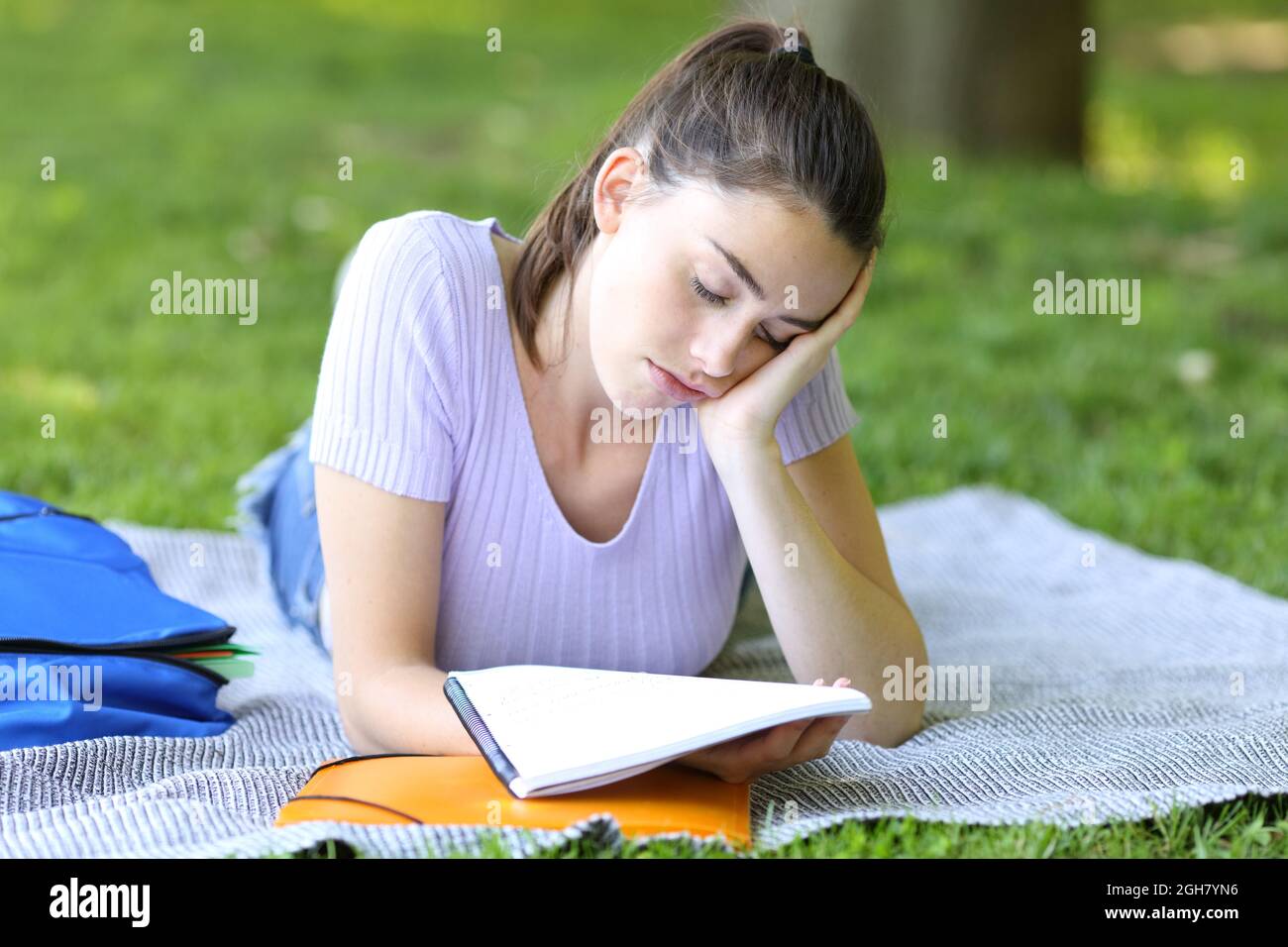 Schlafende Schülerin, die versucht, sich Notizen zu merken, die auf dem Gras in einem Park oder auf dem Campus liegen Stockfoto