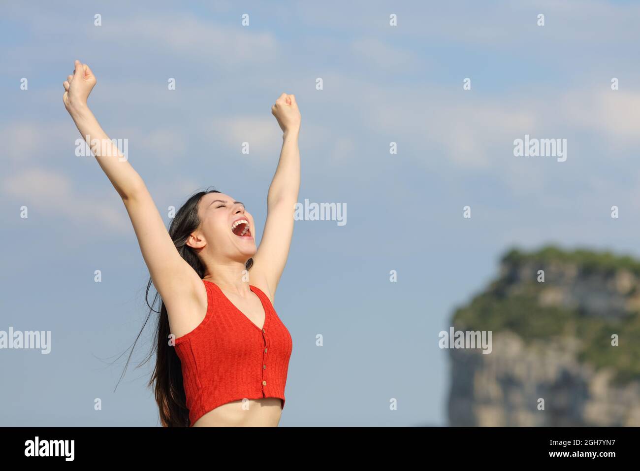 Aufgeregte asiatische Frau in Rot, die die Arme hebt und in der Natur schreit Stockfoto