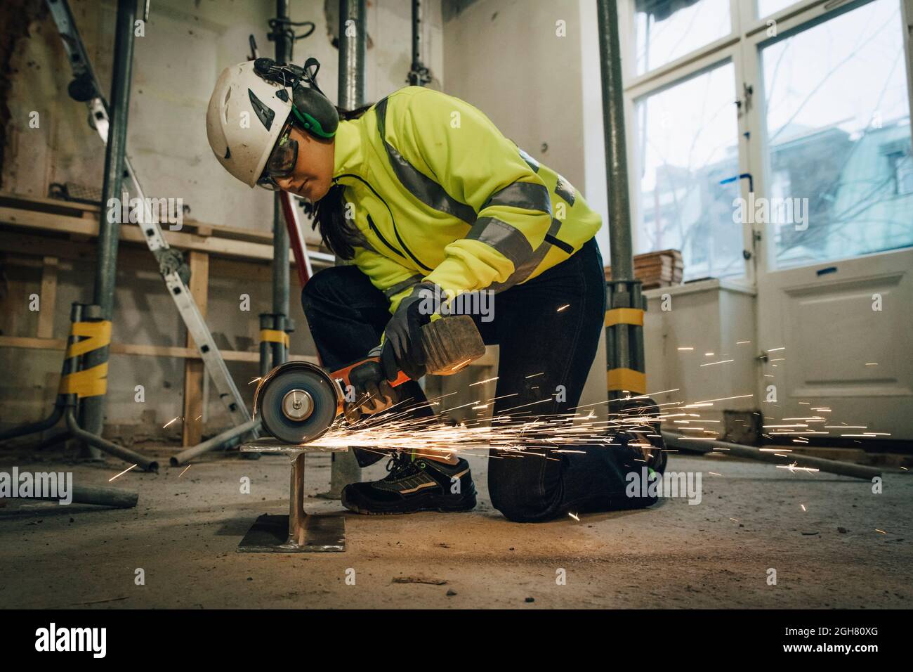 Die gesamte Länge einer Bauarbeiterin, die Metall schneidet, während sie eine elektrische Säge vor Ort verwendet Stockfoto