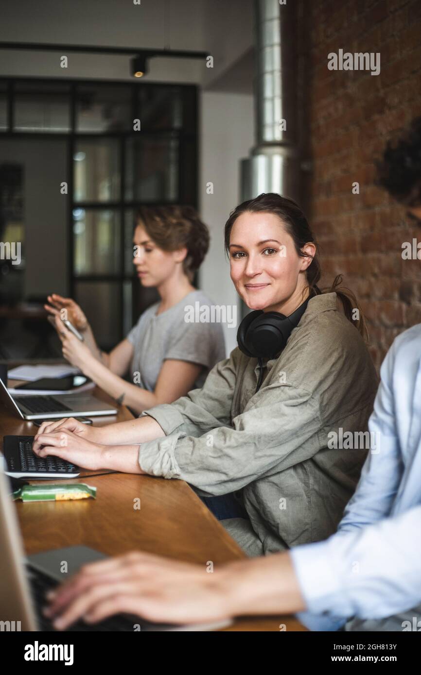 Porträt einer Hackerin, die mit Kollegen im Büro sitzt Stockfoto