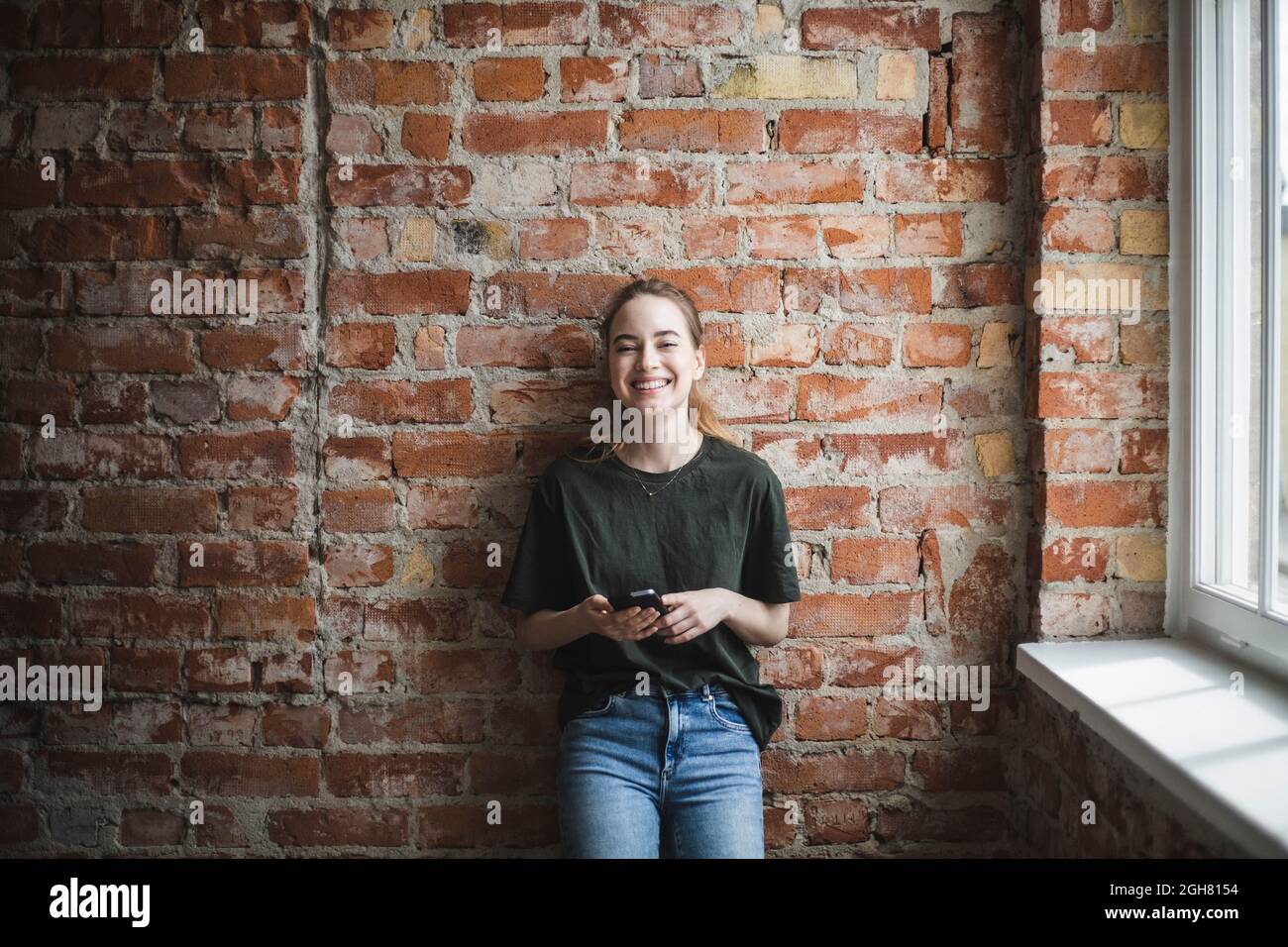 Lächelnde junge Hackerin mit Smartphone im Büro Stockfoto