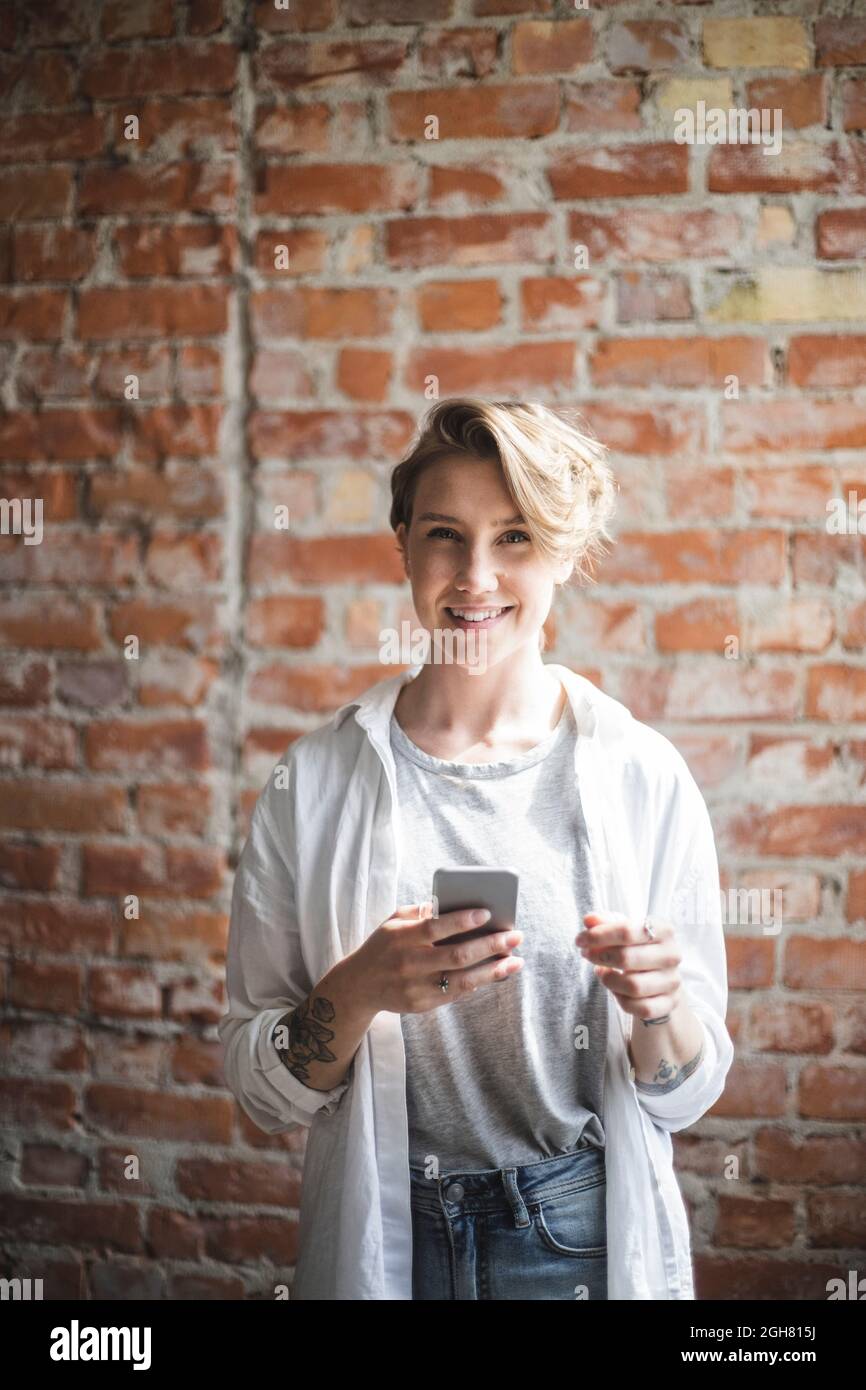 Lächelnde Hackerin mit Smartphone im Startup-Unternehmen Stockfoto