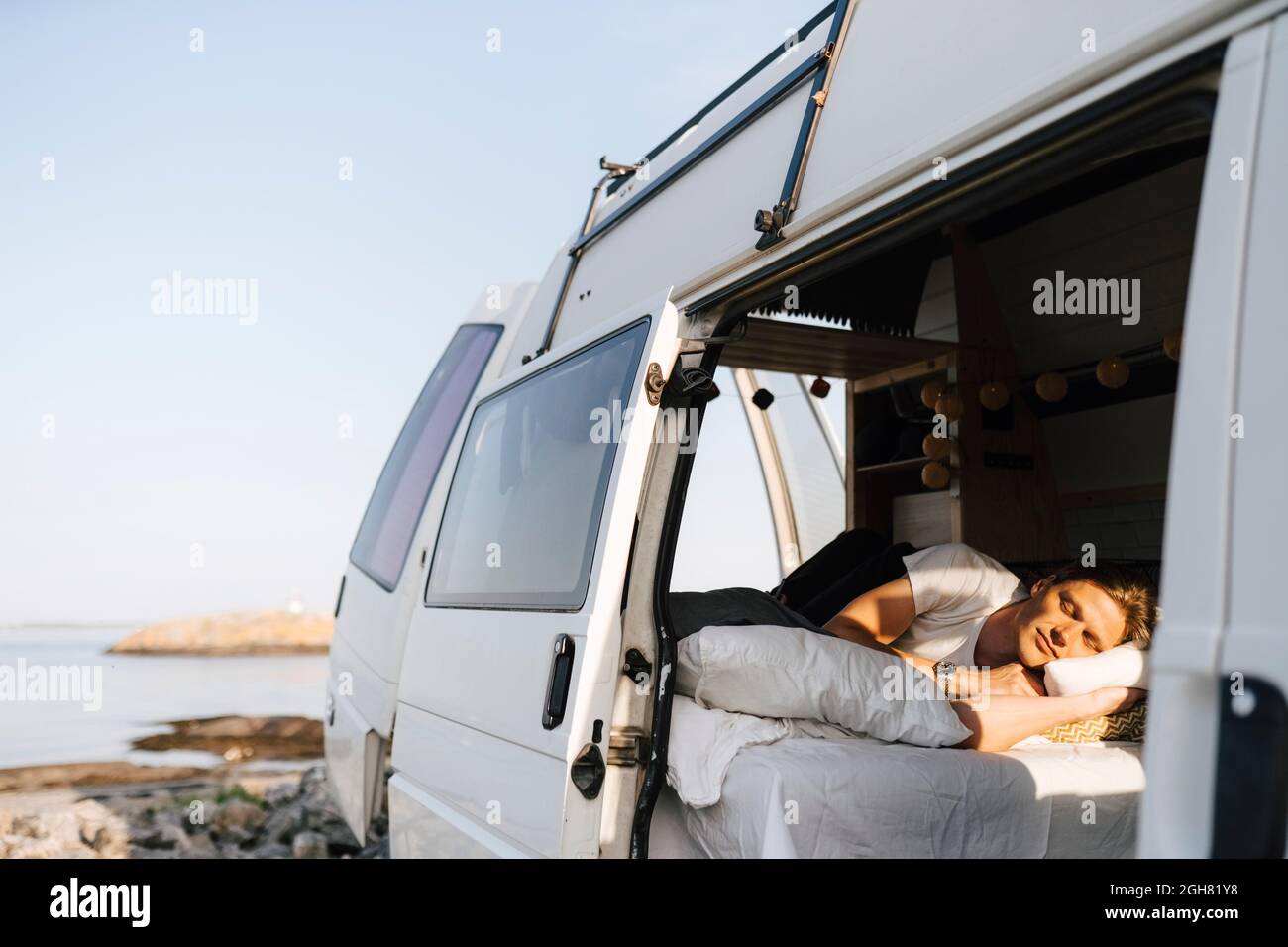 Mann, der sich im Campingbus am Seeufer entspannt Stockfoto