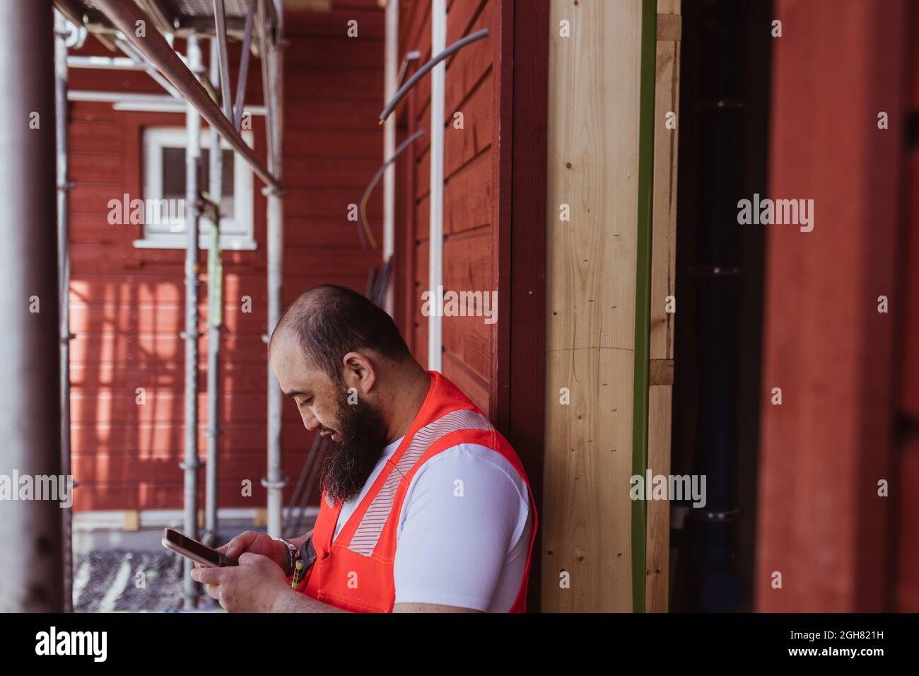Bärtiger Bauarbeiter, der vor Ort ein Smartphone benutzt Stockfoto