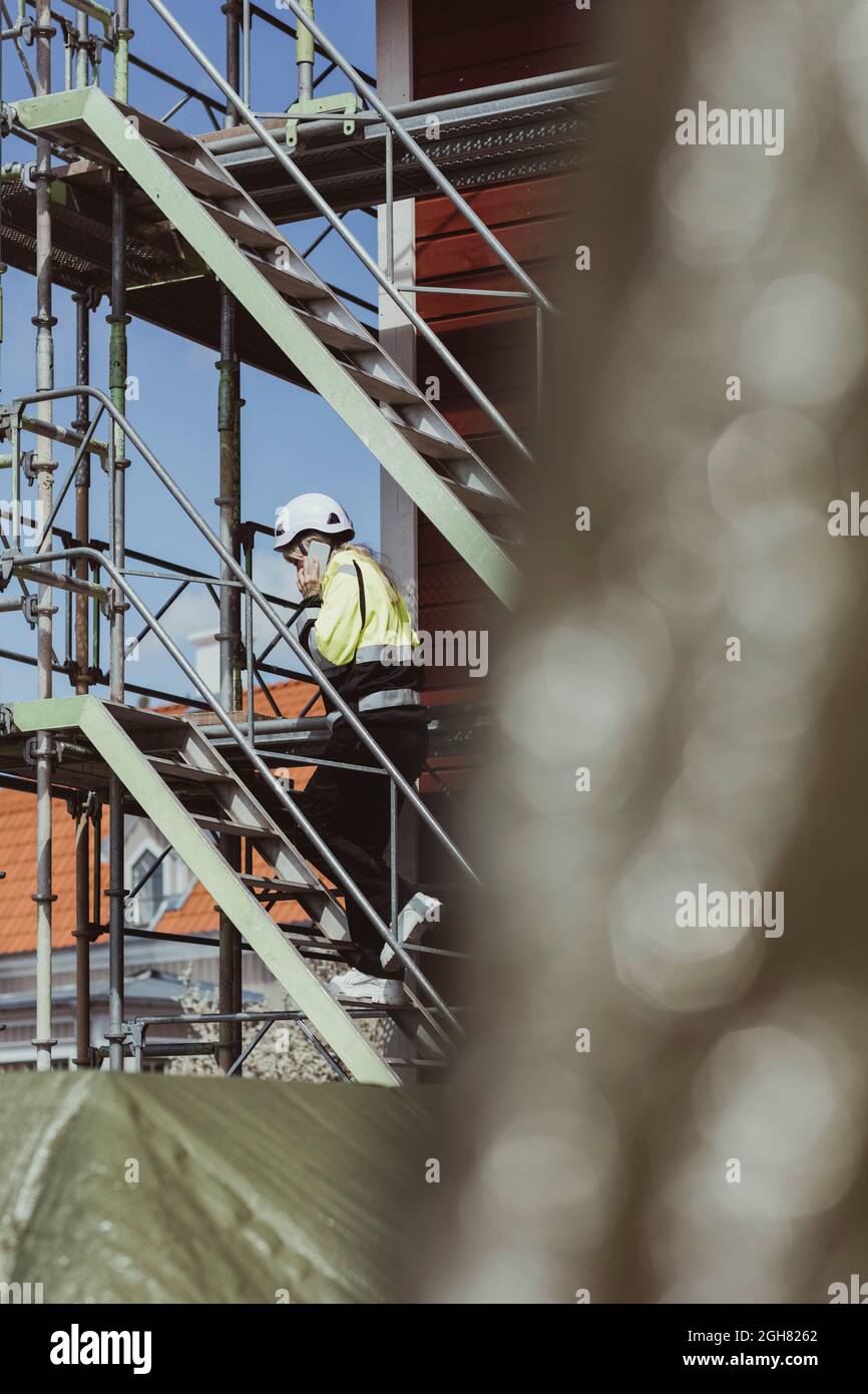 Die gesamte Dauer der Gespräche einer Bauunternehmerin mit einem Smartphone, während sie auf die Stufen auf der Baustelle aufstieg Stockfoto
