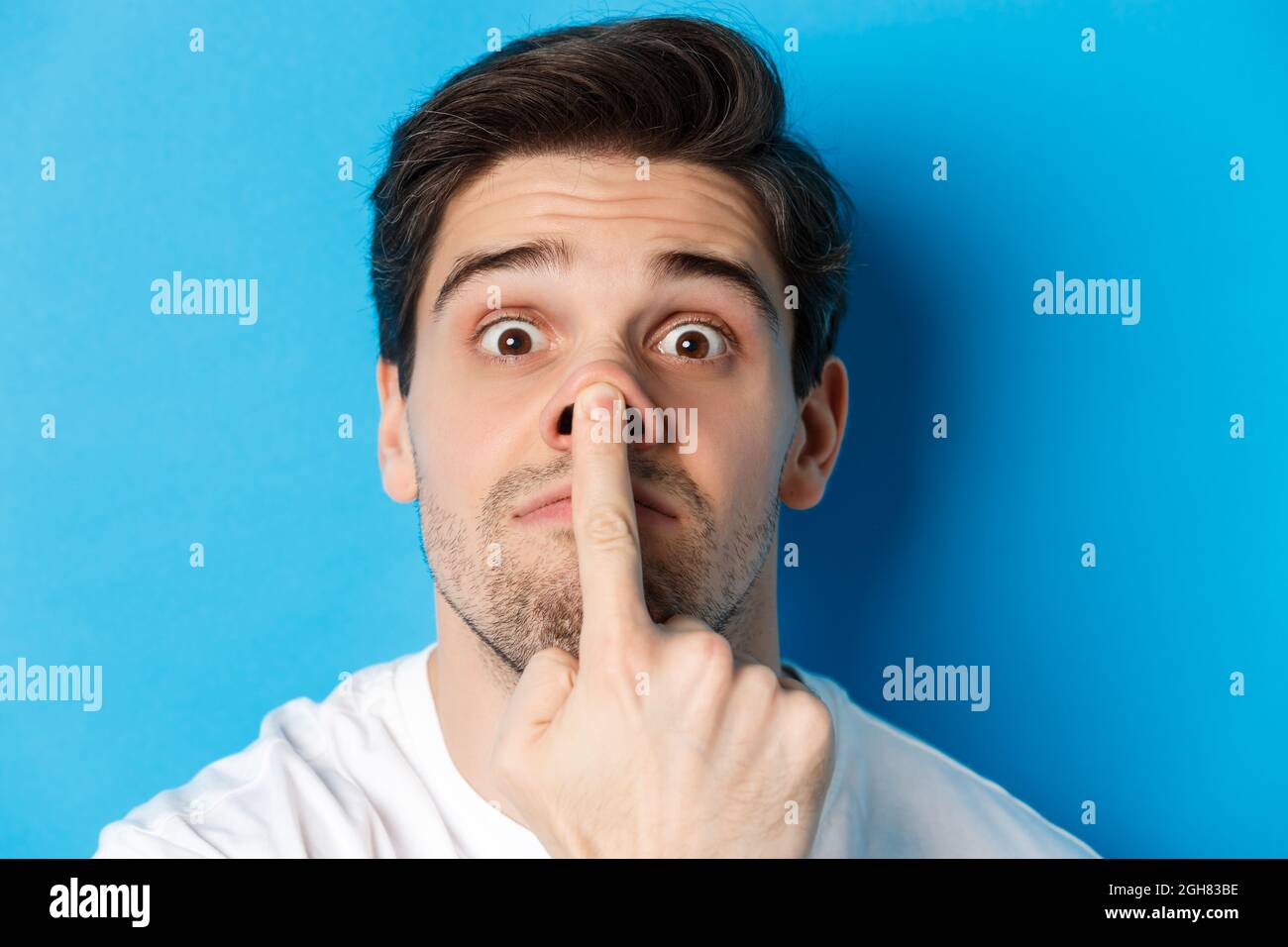 Kopfschuss des kaukasischen Kerl, der lustige Ausdrücke macht, über blauem Hintergrund stehend Stockfoto