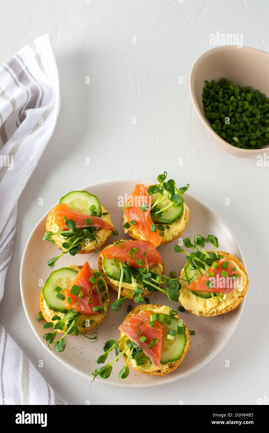 Leckere herzhafte Vorspeise, Lachsbraten auf einem weißen Teller, rundes gebratenes Brötchen mit rotem Fisch, Gurke, Sauce Hollandaise und Erbsensprossen Stockfoto