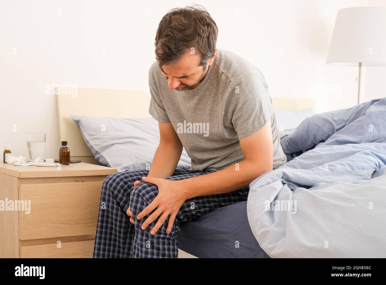 Mann mit Knieschmerzen sitzt auf dem Bett Stockfoto