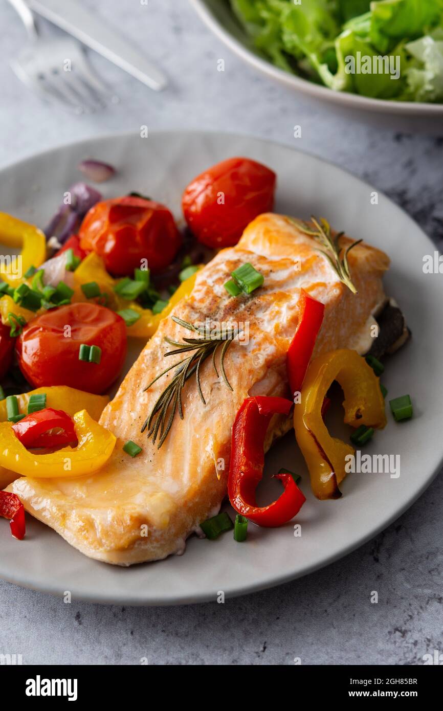 Gebackenes rotes Fischfilet Arctic Saibling auf einem Teller mit Gemüse, Salat in einer Schüssel mischen, leckeres herzhaftes gesundes Abendessen Stockfoto