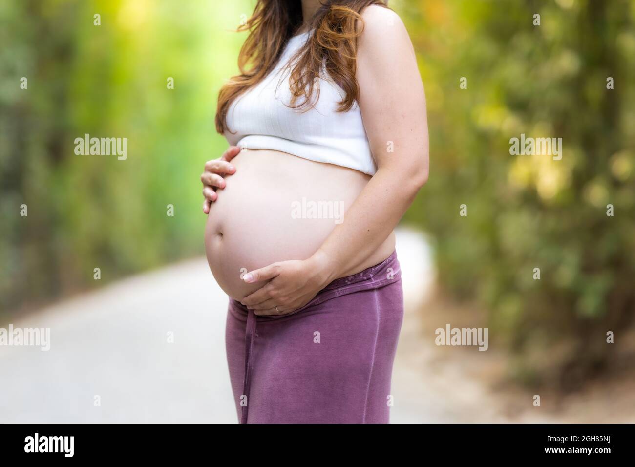 Nahaufnahme der Hände einer erwachsenen Schwangeren in ihrem Bauch im Freien Stockfoto