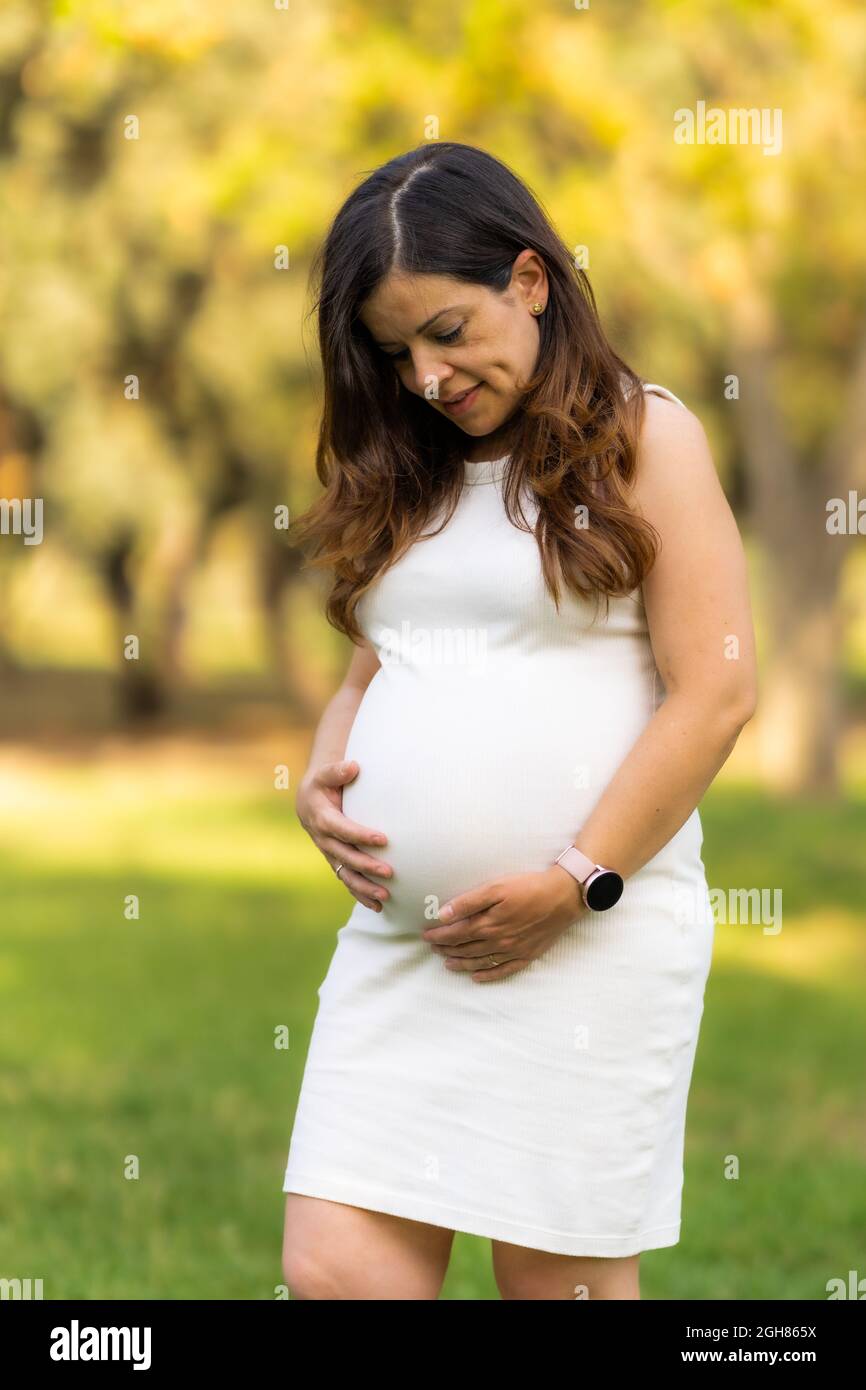 Vertikales Foto einer Frau, die steht und ihren Bauch anschaut, während sie ihn berührt Stockfoto