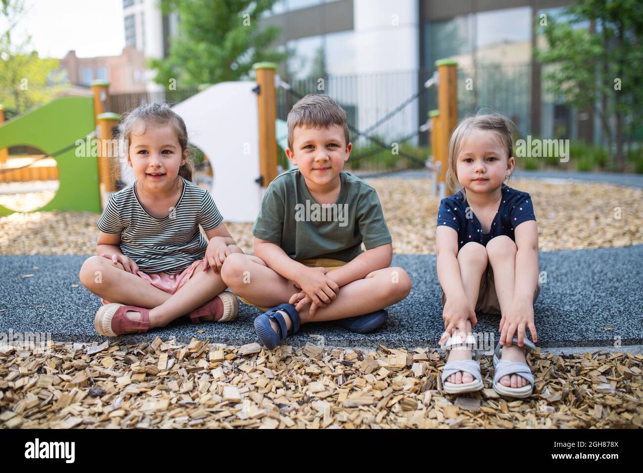 Gruppe von kleinen Kindern im Kindergarten, die draußen auf dem Spielplatz sitzen und die Kamera betrachten. Stockfoto