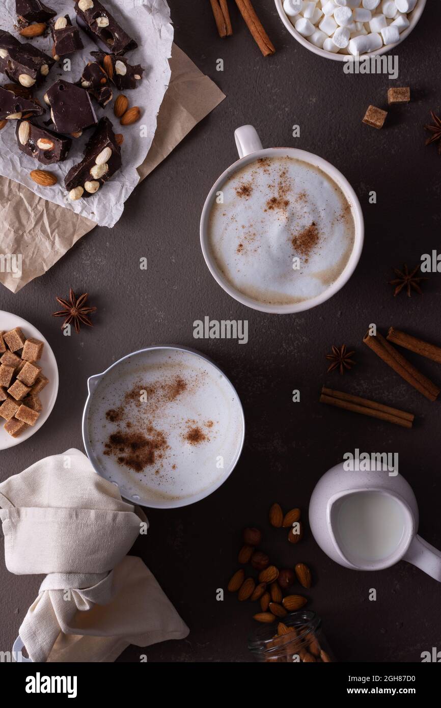 Winterkakaogetränk mit Milchschaum und Moorsalbe in einem Becher und einer Aluminiumlöffel, Zimt und Mandeln, dunkler Schokolade mit Nüssen Stockfoto