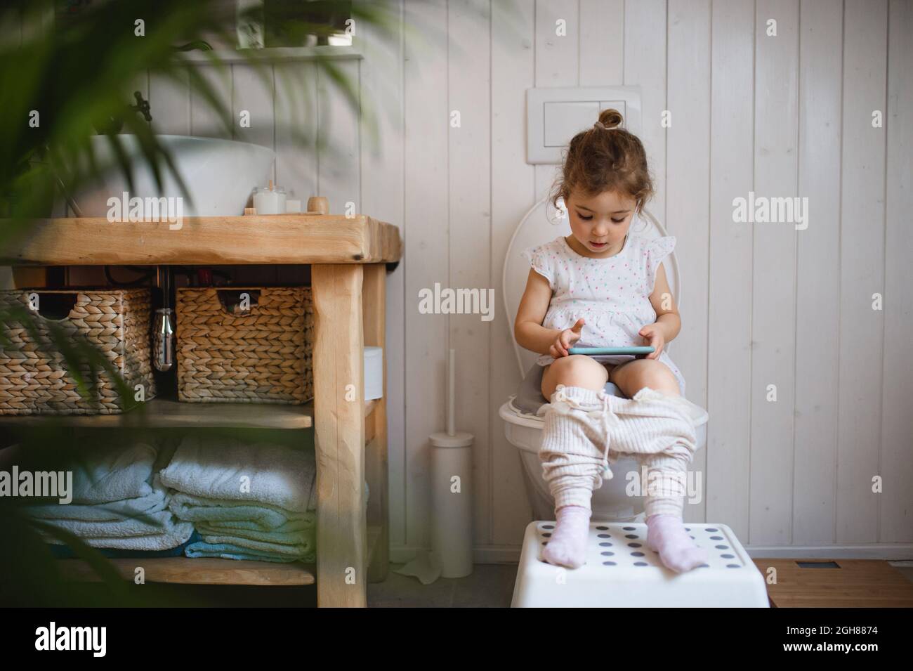 Portrait of cute small sitting on toilet indoor at Home, using Smartphone. Stockfoto