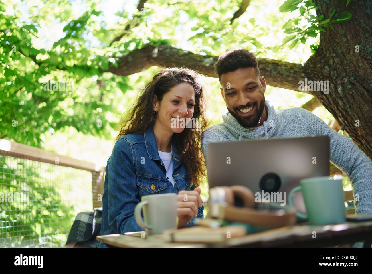 Glückliches Paar mit einem Laptop, der sich im Freien in einem Baumhaus, einem Wochenendausflug und einem Remote-Office-Konzept ausruhen kann. Stockfoto
