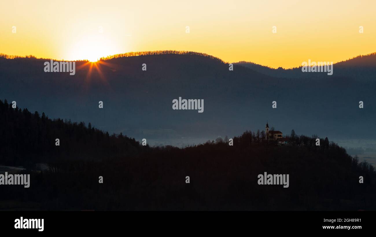 Sonnenuntergang hinter der Kirche von Marija (Sveta Marija) und ihrem Hügel auf den Ljubjana Mauren, Slowenien. Von der Kirche der Heiligen Anna (Sveta Ana) aus gesehen. Sveta Stockfoto