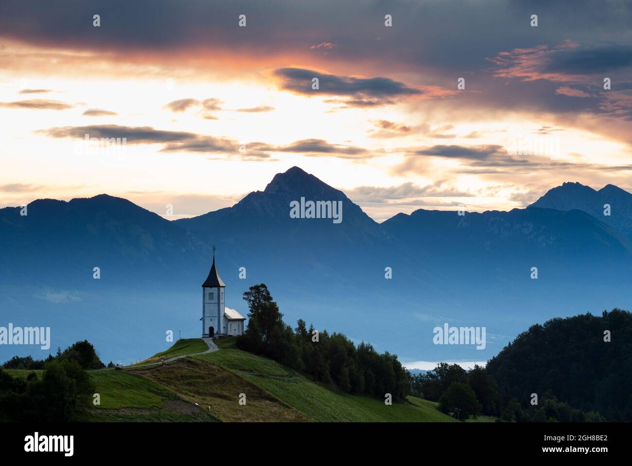 Jamnik Kirche des Heiligen Primus und Felician, thront auf einem Hügel auf der Jelovica Hochebene mit den Steiner Alpen und Storzic Berg im Hintergrund, Sl Stockfoto