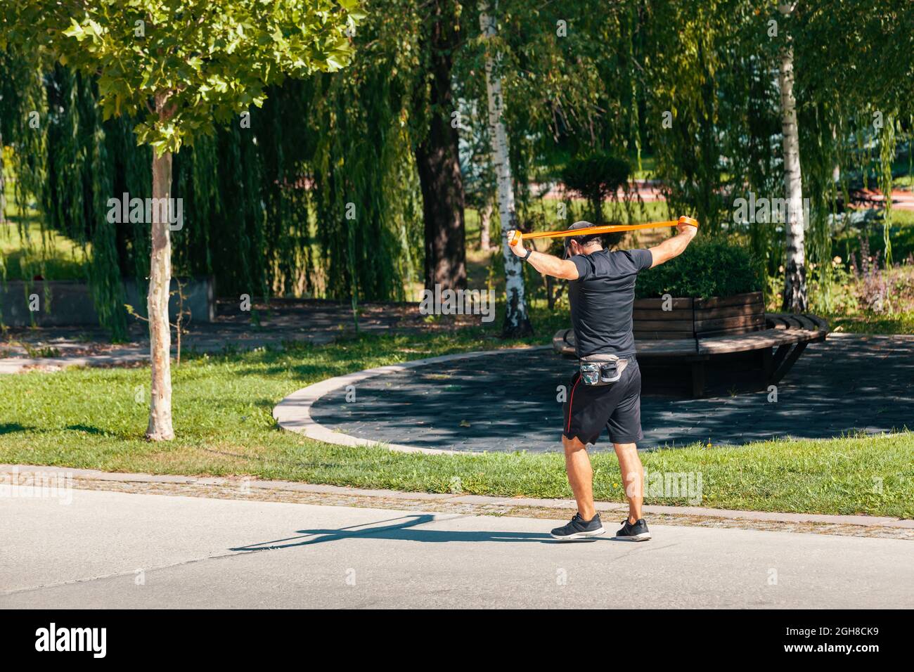 Ankara, Türkei - 02. September 2021: Junger Mann, der an einem sonnigen Morgen in D durch den Park spazierengeht und mit einer Widerstandsband-Pilates-Bewegung trainiert Stockfoto