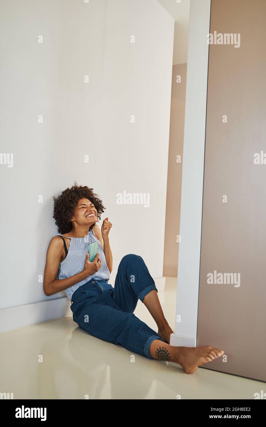 Strahlende Frau mit ihrem Smartphone an der Wand sitzend Stockfoto